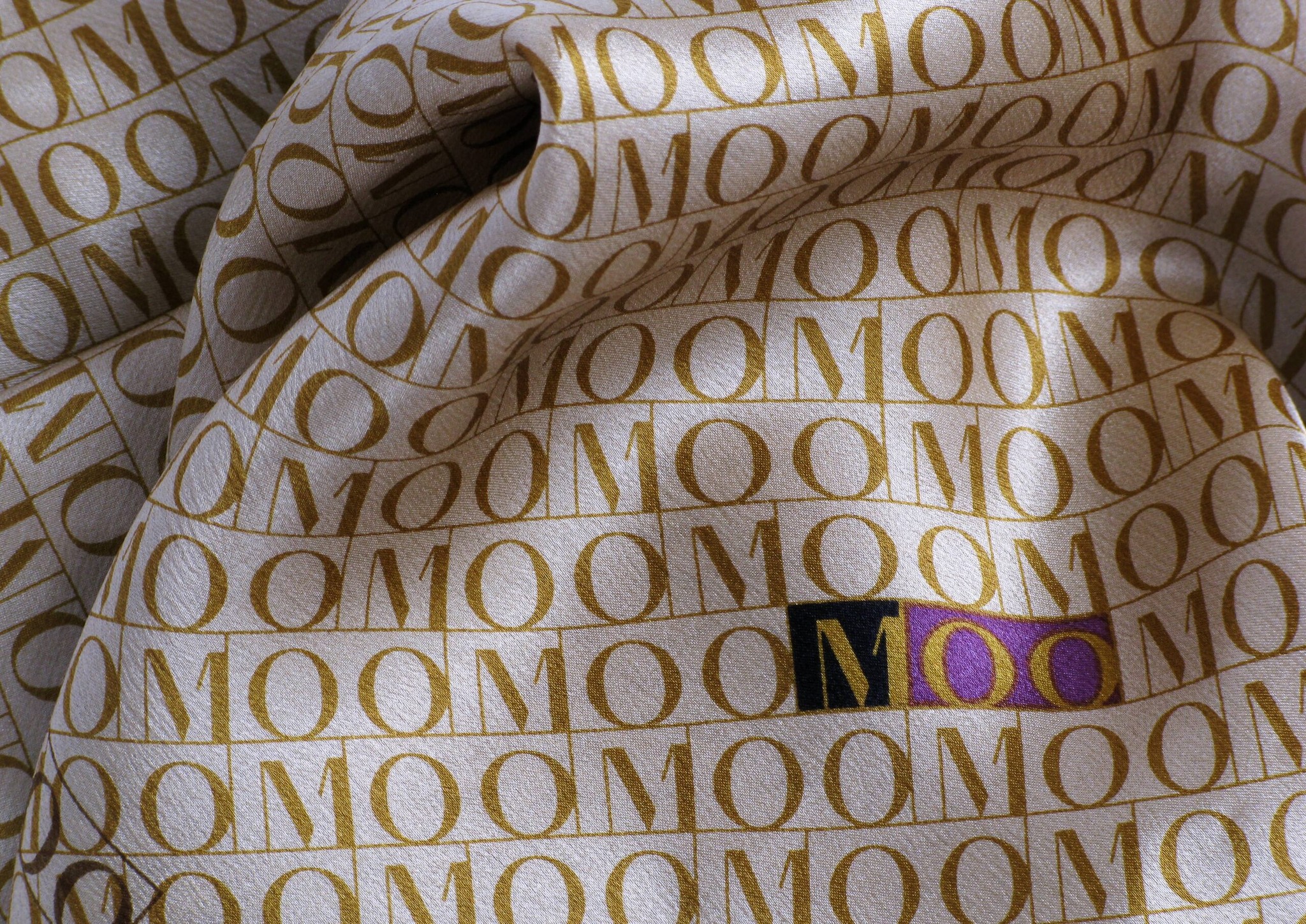 Fabric printed with repeating gold MOO lettering, a woven label at its centre