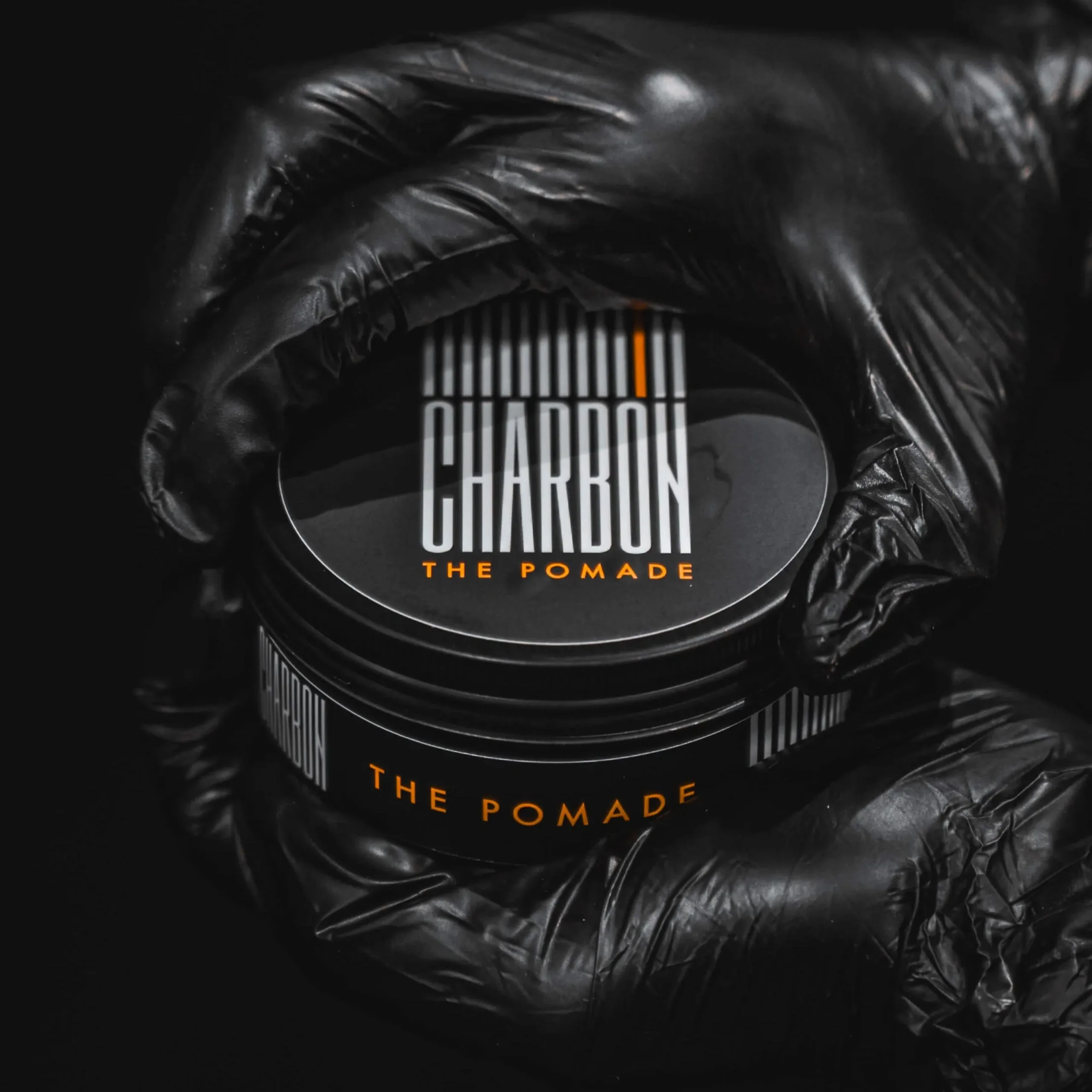 A tin of Charbon pomade held in a black-gloved hand